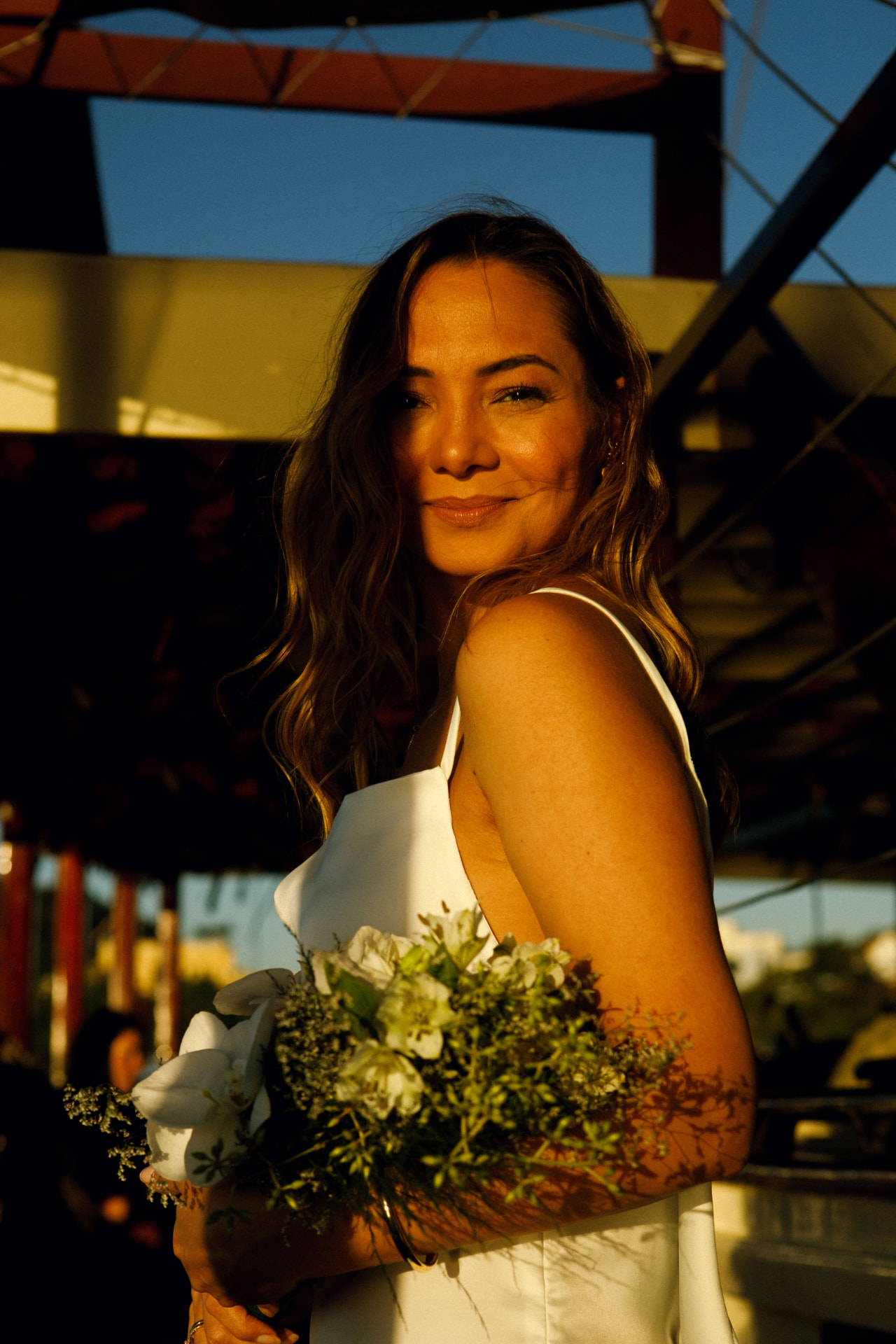 Noiva com buquê de flores brancas sorrindo na luz dourada do fim de tarde a bordo do saveiro